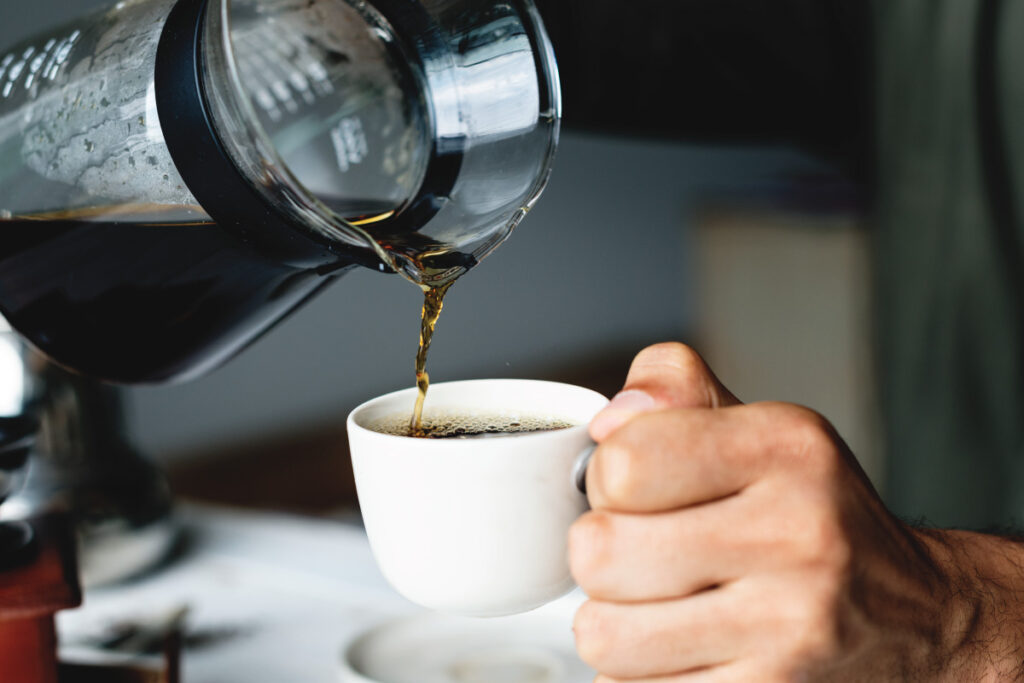 pouring black coffee from a big glass jar into casual white coffee cup